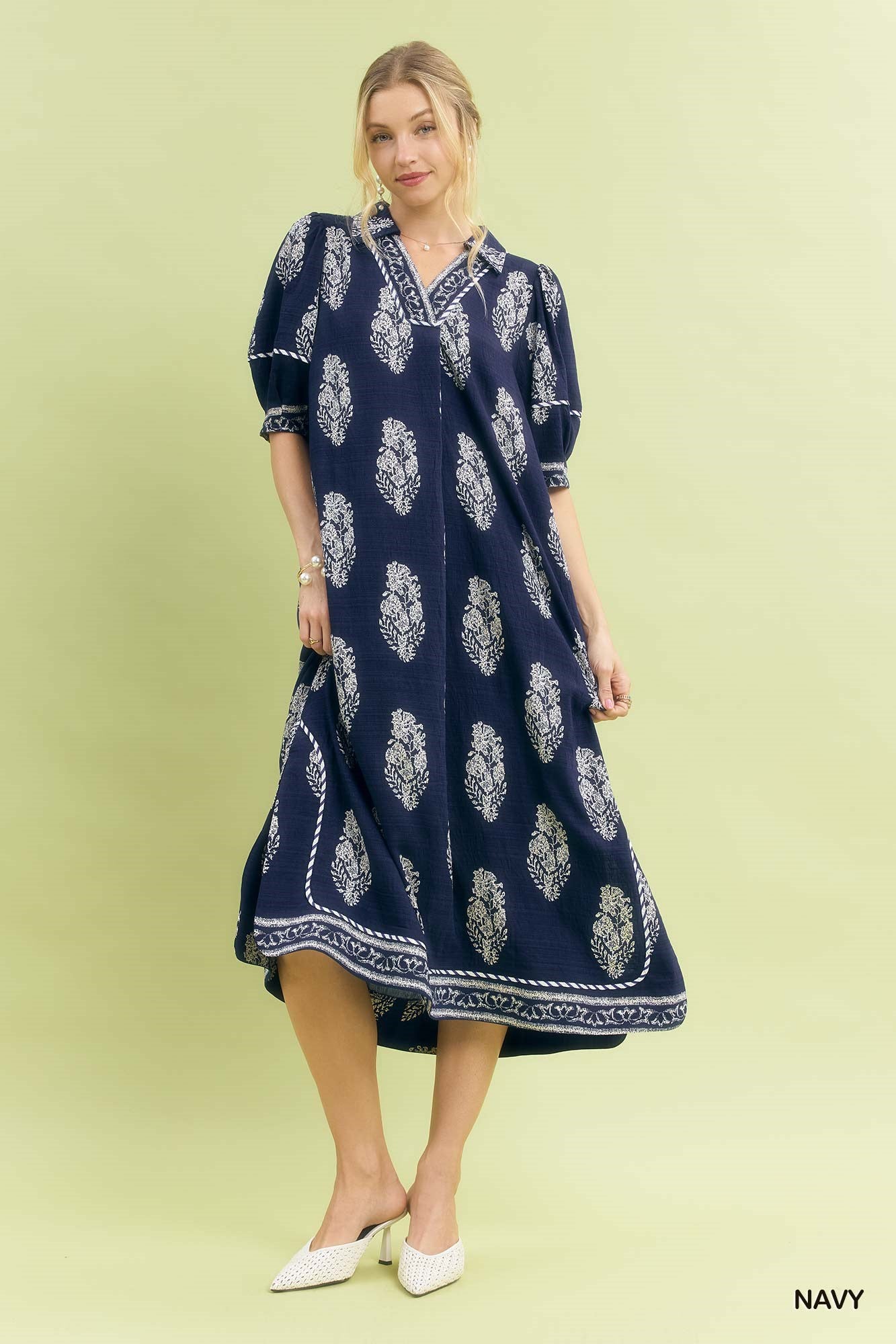 Woman wearing a navy dress with white floral pattern on a light green background