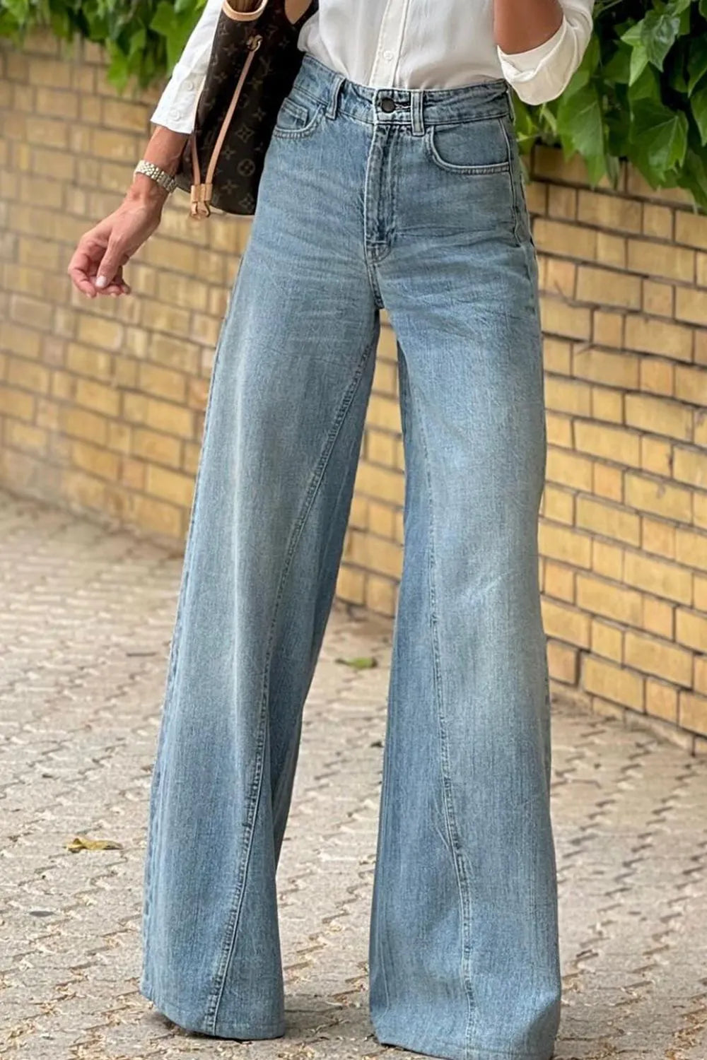 Person wearing light blue wide-leg jeans against a brick wall.