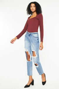 Woman wearing a burgundy long-sleeve top and light blue ripped jeans on a white background