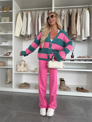 Woman in a pink and green striped cardigan and pink pants standing in a wardrobe with clothes and shoes on shelves.
