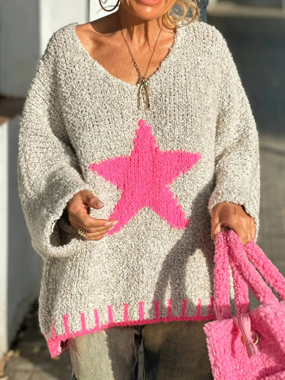 Person wearing a gray sweater with a pink star design, holding a pink bag.