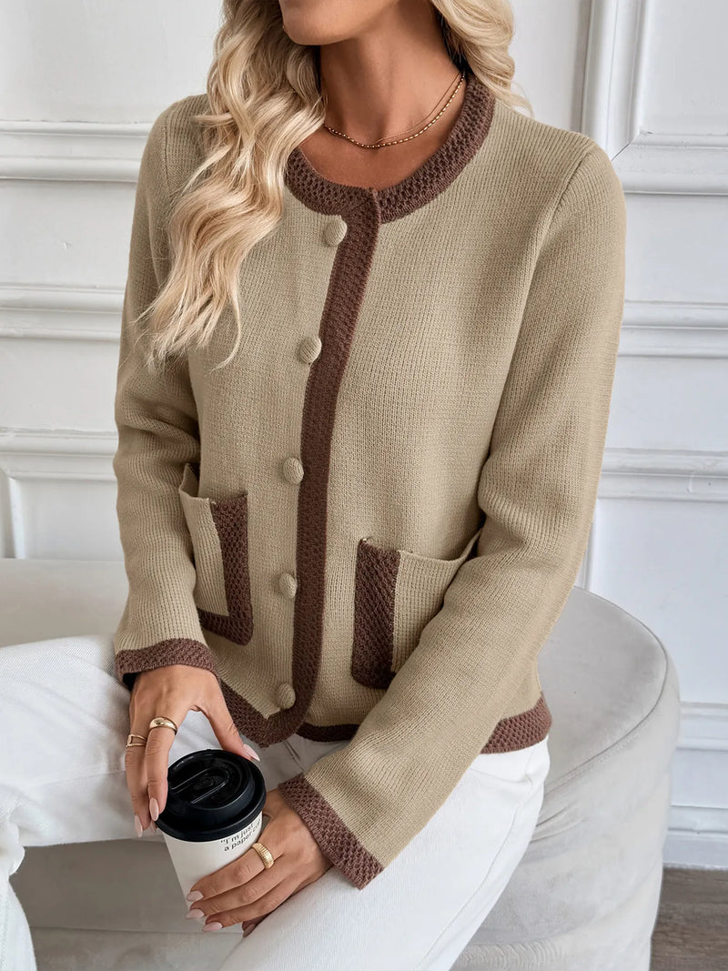 Woman wearing a beige sweater with brown accents, sitting on a white chair.