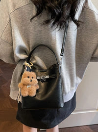 Person wearing a gray sweatshirt with a black backpack featuring a teddy bear keychain.
