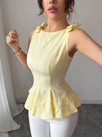Woman wearing a yellow peplum top with decorative bows on a plain background