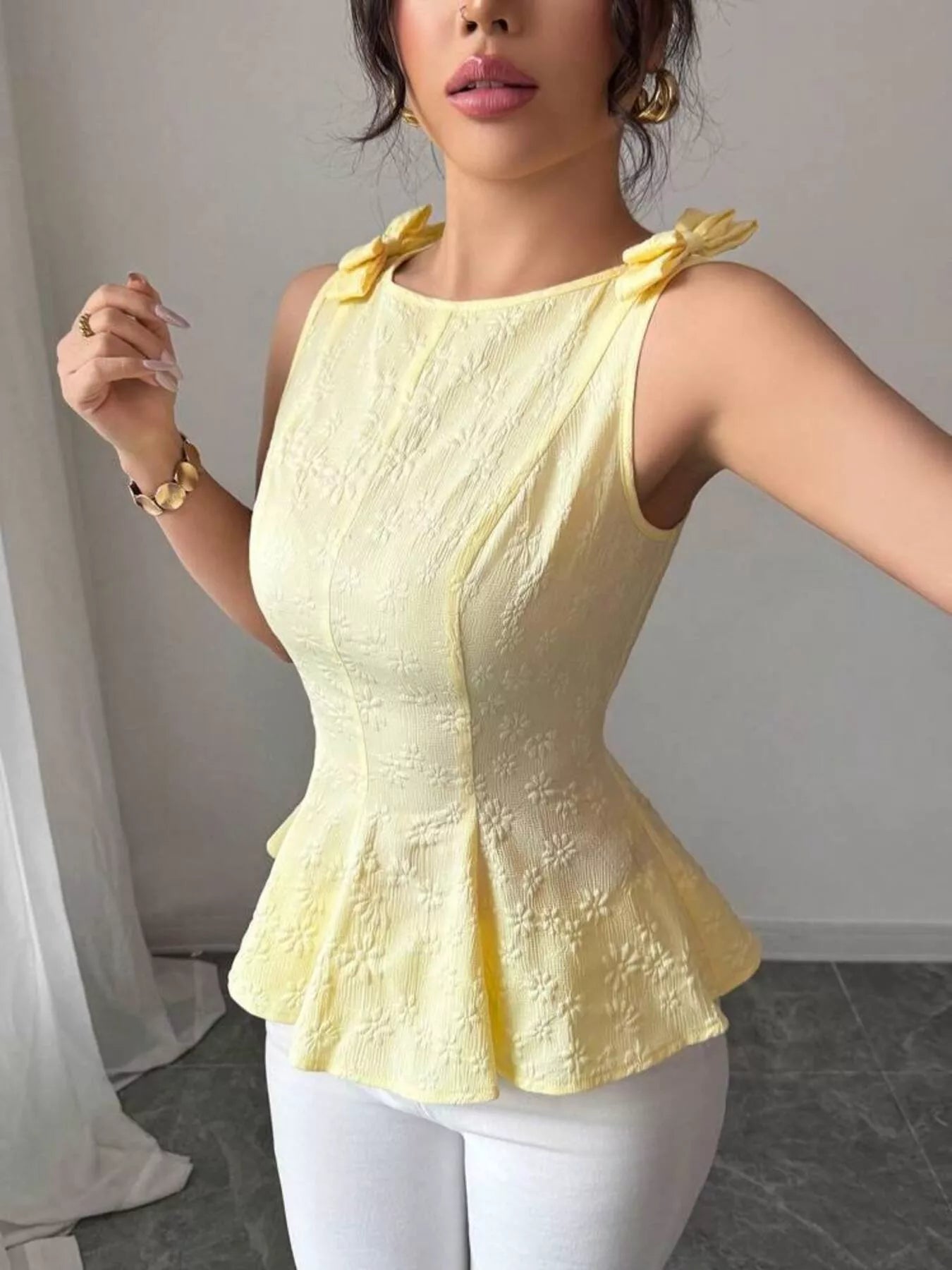 Woman wearing a yellow peplum top with decorative bows on a plain background