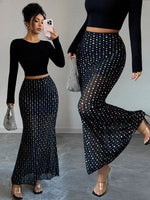 Woman wearing a black long-sleeve top and black polka dot skirt, holding a phone and clutch.