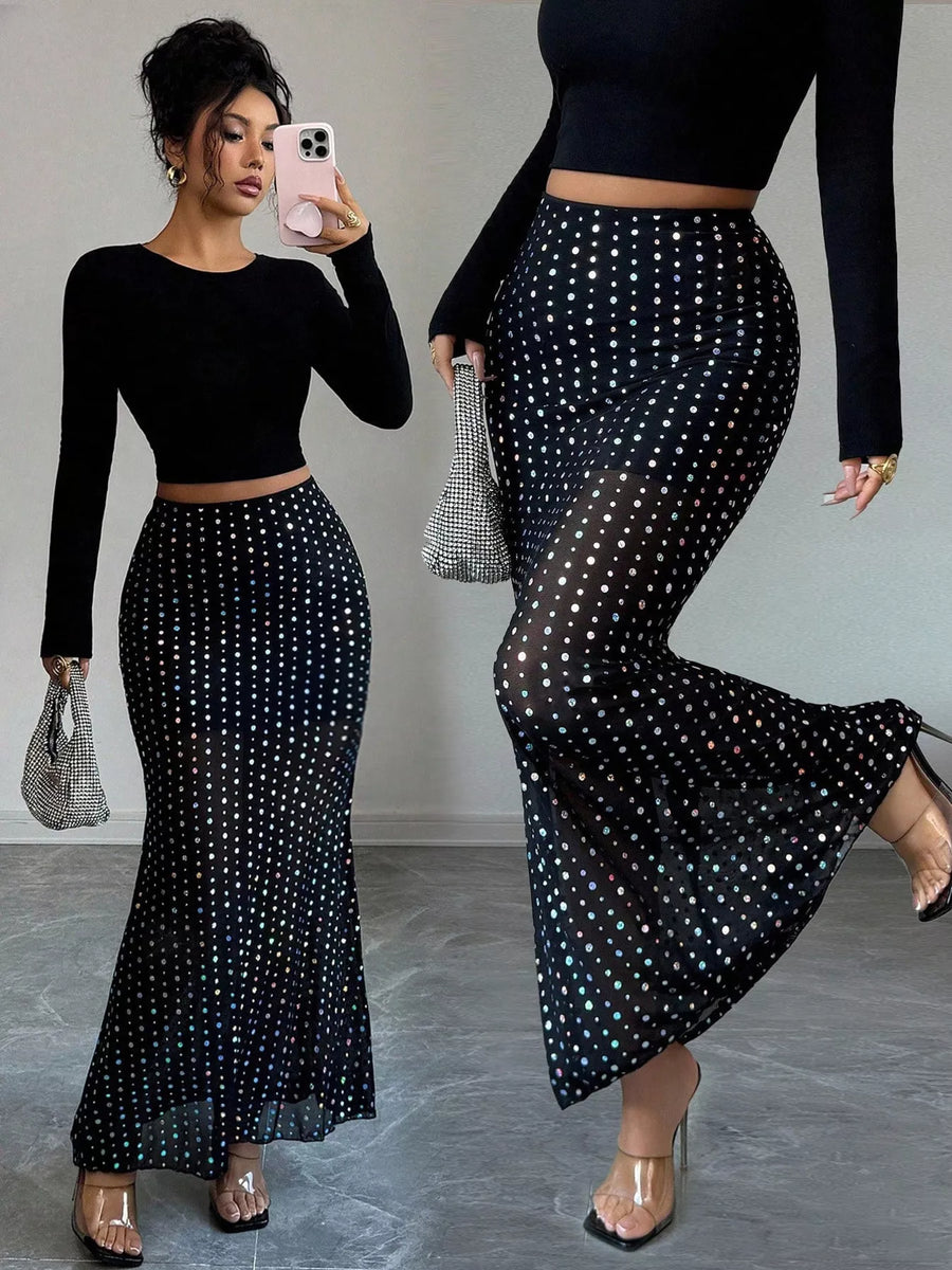 Woman wearing a black long-sleeve top and black polka dot skirt, holding a phone and clutch.