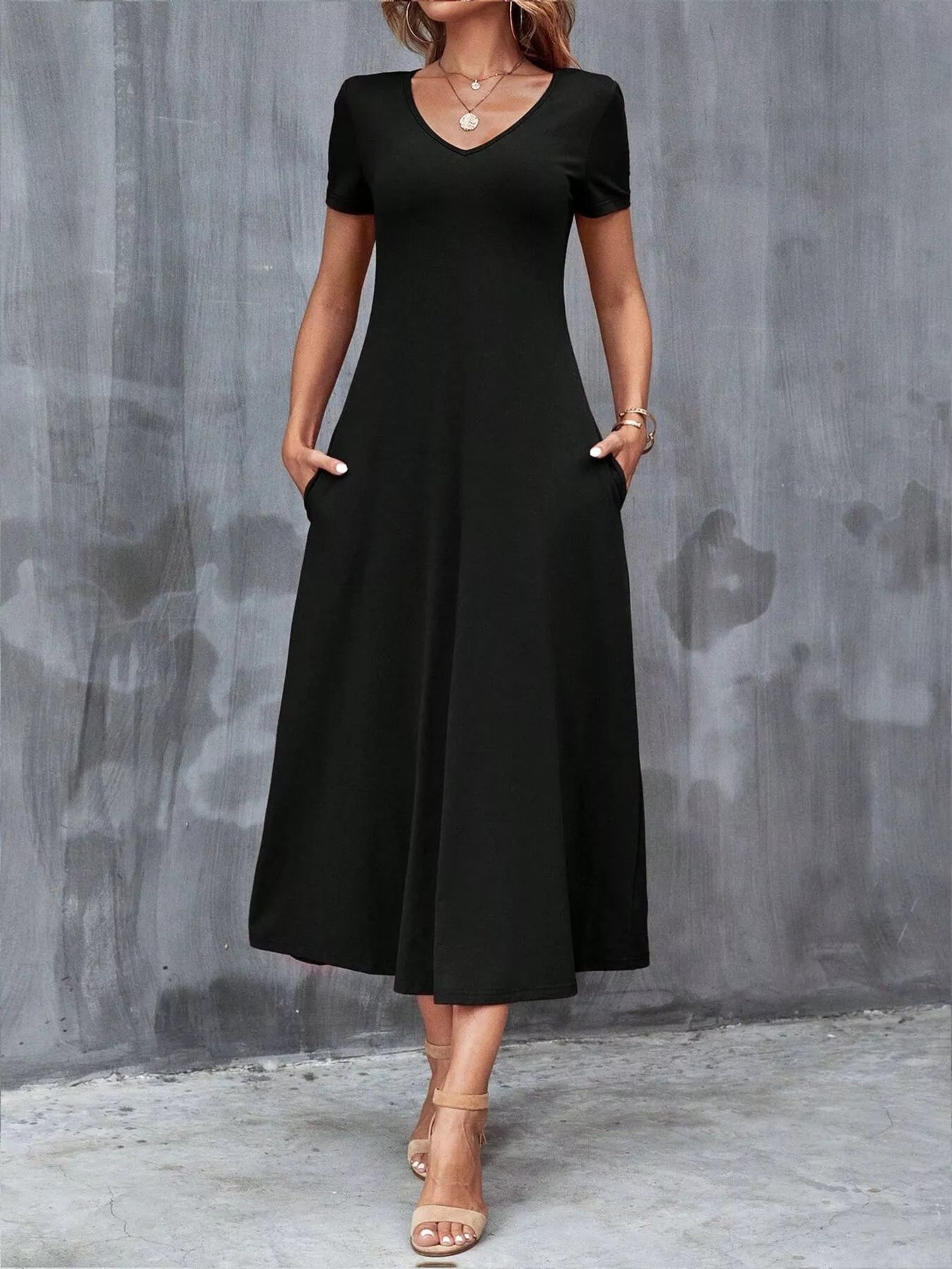 Woman wearing a black dress against a gray concrete wall.