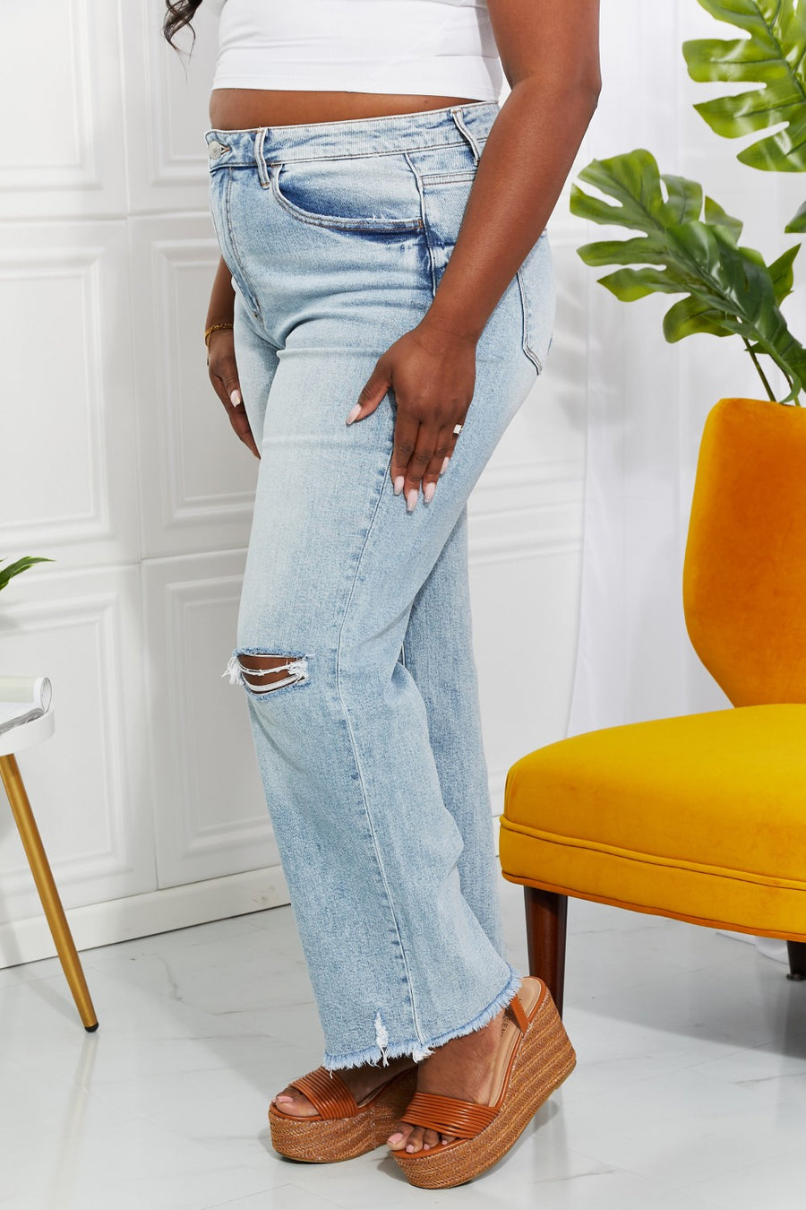 Person wearing light blue jeans with a white background and yellow chair.