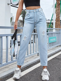 Person wearing light blue distressed jeans and white sneakers on a street.