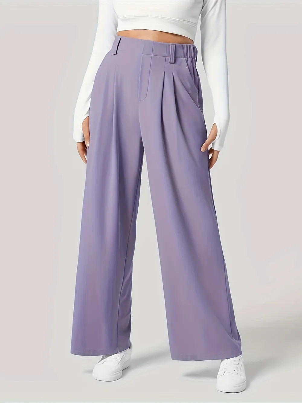 Person wearing lavender wide-leg pants with a white top and sneakers on a light gray background