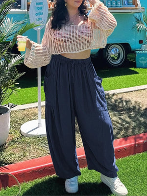 Person wearing a beige crochet top and navy pants standing outdoors with a colorful vehicle in the background.