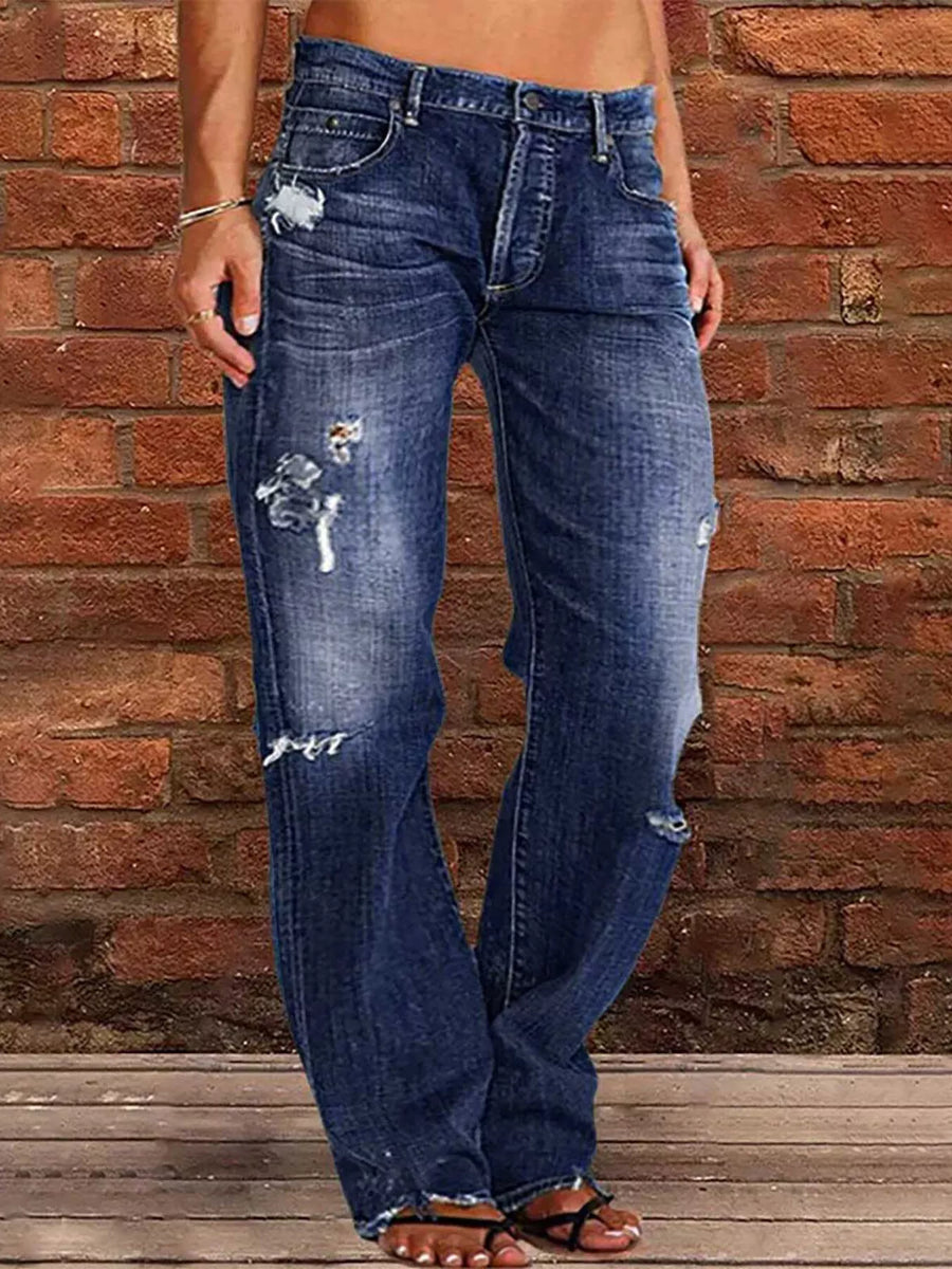 Person wearing distressed blue jeans against a brick wall.