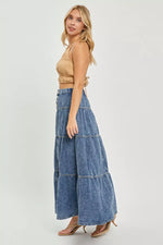 Woman wearing a beige top and blue tiered denim pants on a white background