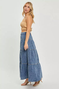 Woman wearing a beige top and blue tiered denim pants on a white background