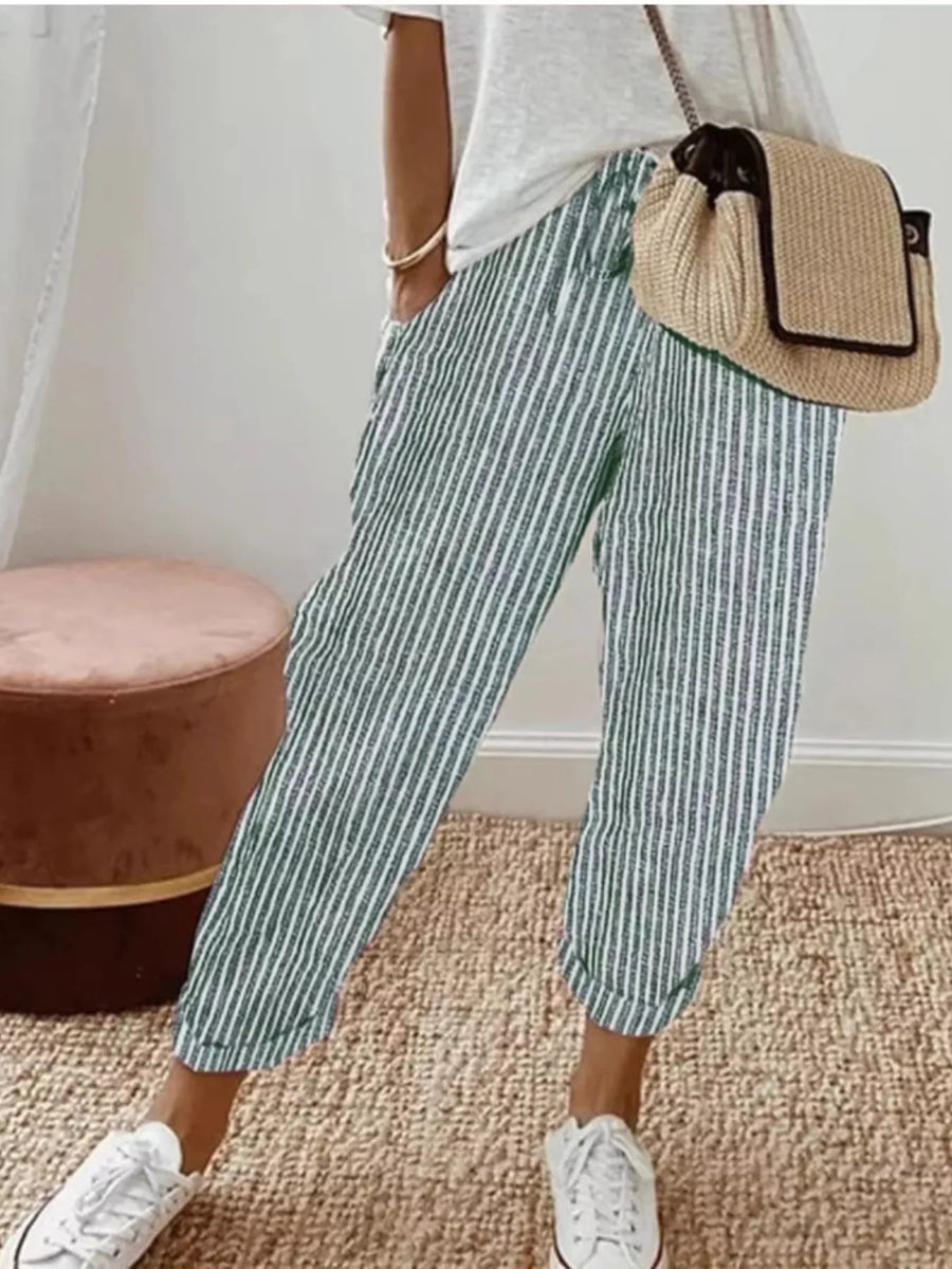 Person wearing green and white striped pants with a beige bag indoors.