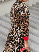 Person wearing a leopard print dress with a red sleeve and holding a gold handbag on a staircase.