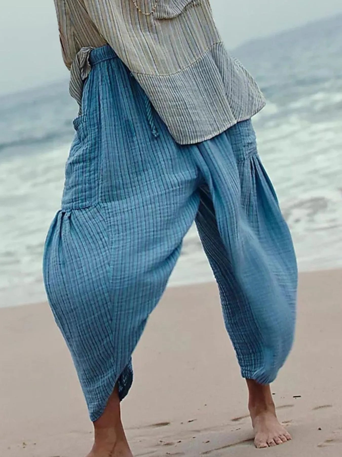 Person wearing blue checkered pants and a striped shirt on a beach.