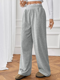 Person wearing gray sweatpants in a room with white curtains and wooden floor.