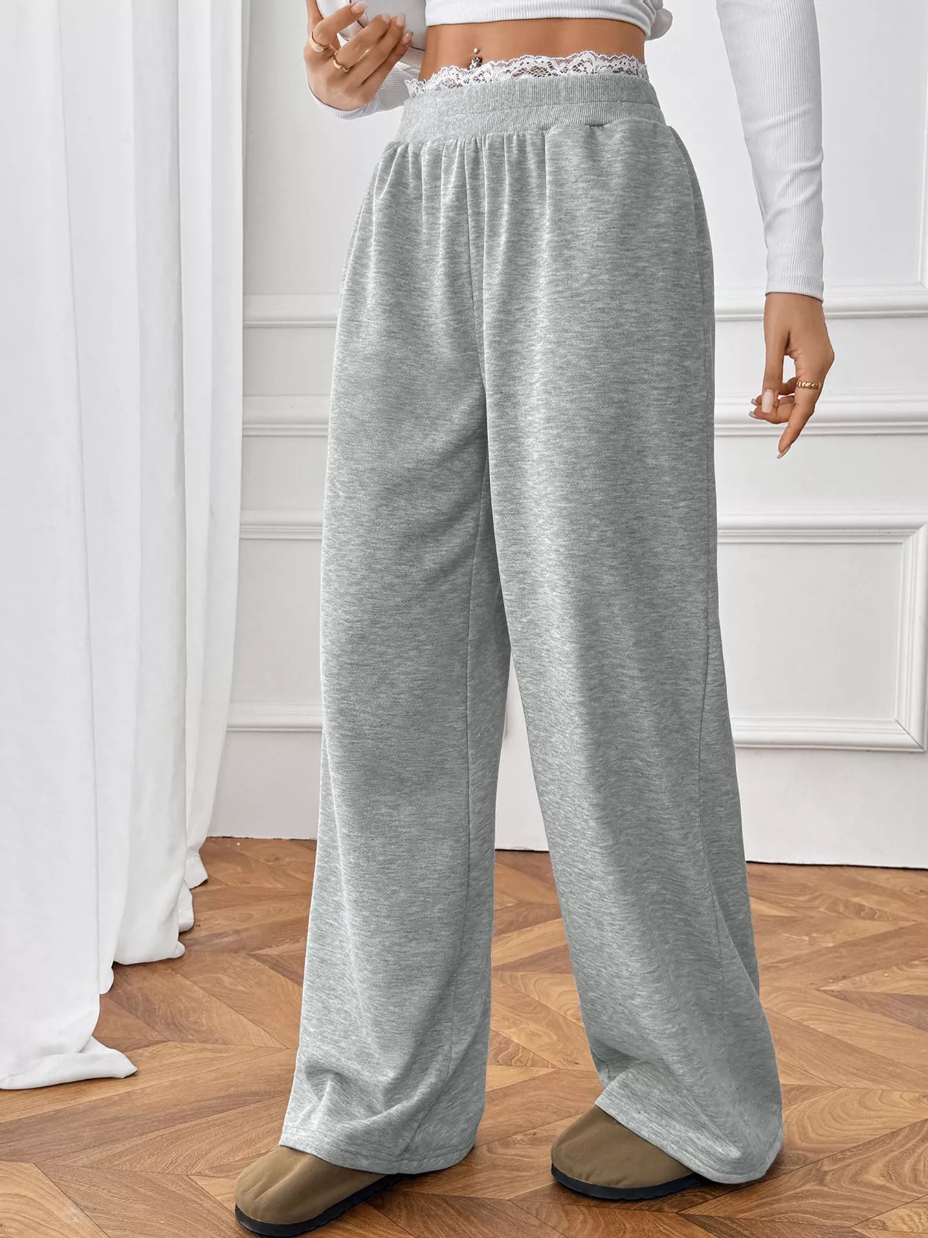 Person wearing gray sweatpants in a room with white curtains and wooden floor.