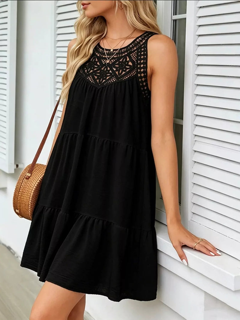 Woman wearing a black dress with lace details, standing against a white wall.