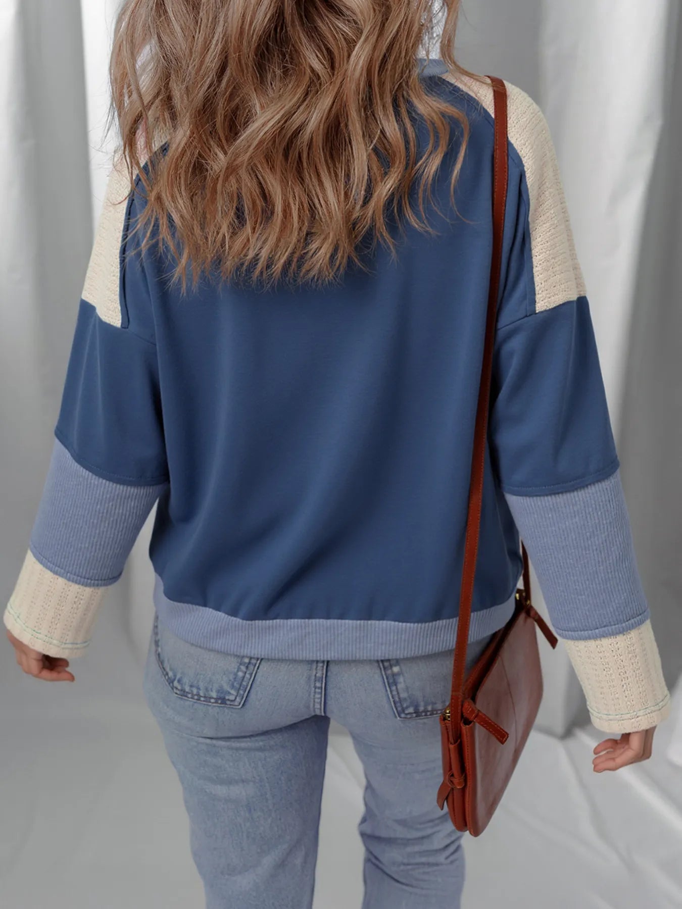 Person wearing a blue and beige jacket with a brown bag on a plain background