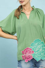 Woman wearing a green blouse with floral designs on a light blue background