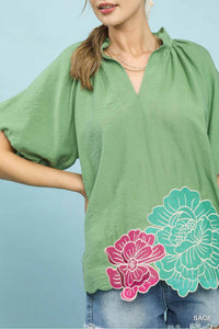 Woman wearing a green blouse with floral designs on a light blue background