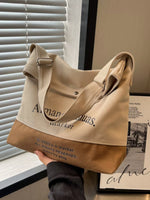 Beige and brown tote bag held by a person with visible branding, against a neutral background.