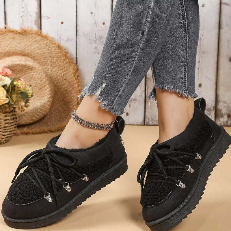 Black lace-up shoes worn with jeans on a wooden floor.