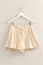 Beige satin shorts on a hanger against a beige wall