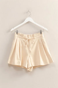 Beige satin shorts on a hanger against a beige wall