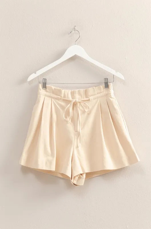 Beige satin shorts on a hanger against a beige wall