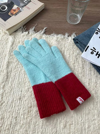 Pair of light blue and red gloves on a textured surface with a book and glass in the background.
