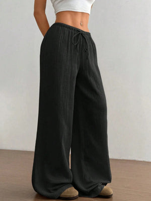 Person wearing black wide-leg pants with a plain background
