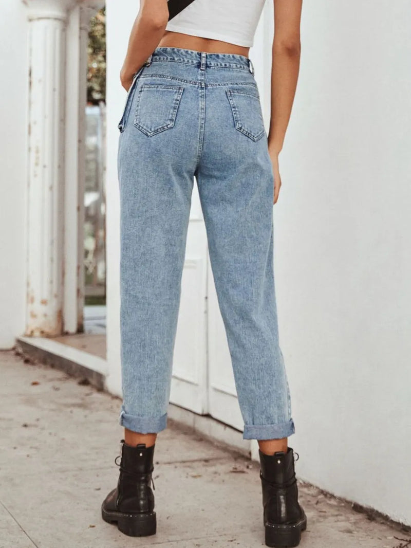 Person wearing light blue jeans and black boots standing on a wooden floor.