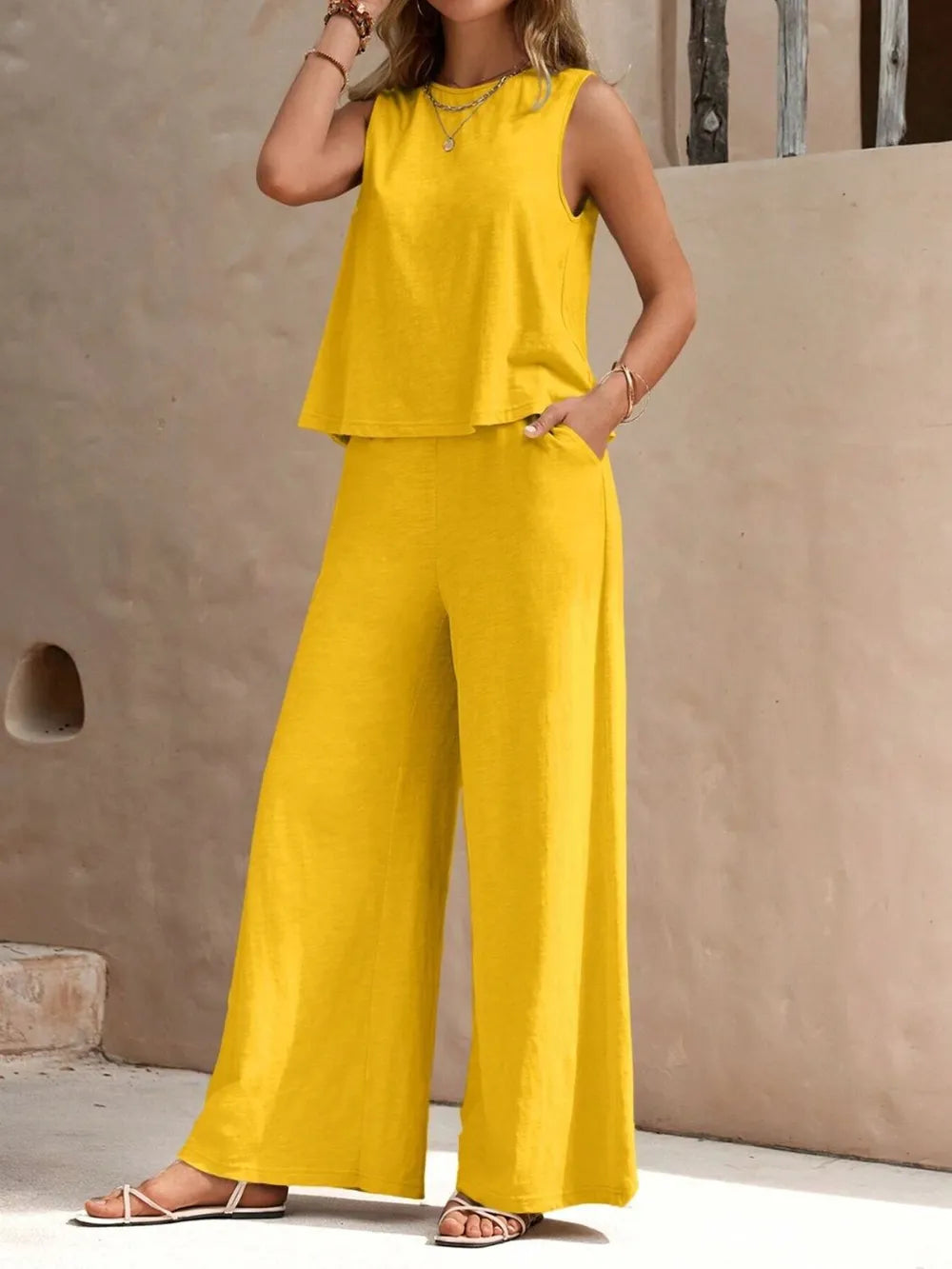 Woman wearing a yellow sleeveless top and wide-leg pants against a beige wall.