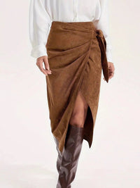 Brown suede wrap skirt worn with a white blouse and brown knee-high boots on a white background