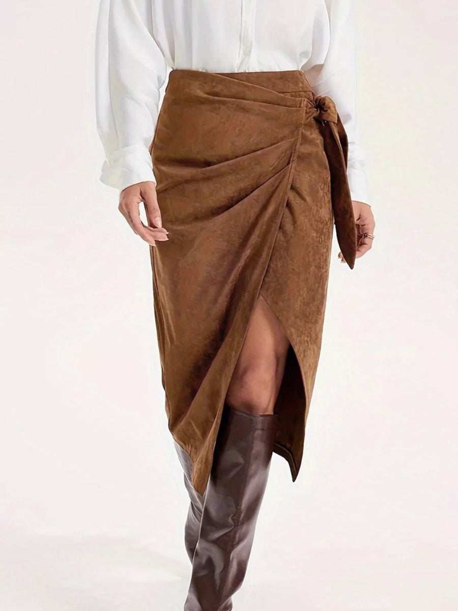 Brown suede wrap skirt worn with a white blouse and brown knee-high boots on a white background