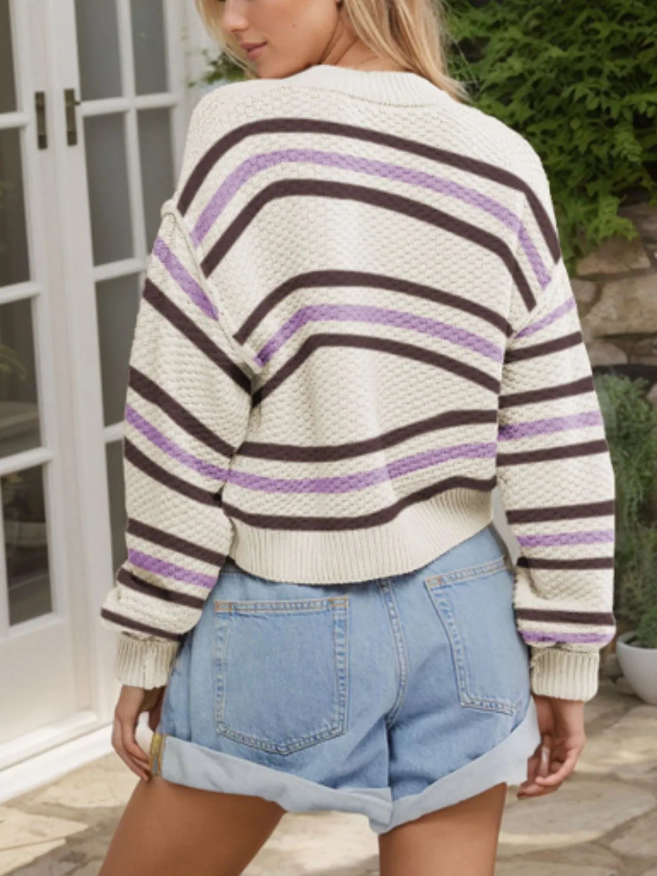Person wearing a striped sweater and denim shorts outdoors.
