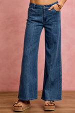 Person wearing blue wide-leg jeans against a pink background