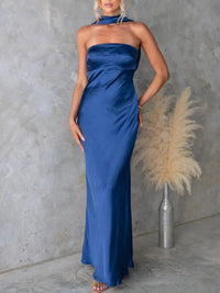 Woman wearing a blue halter neck gown against a gray concrete wall.