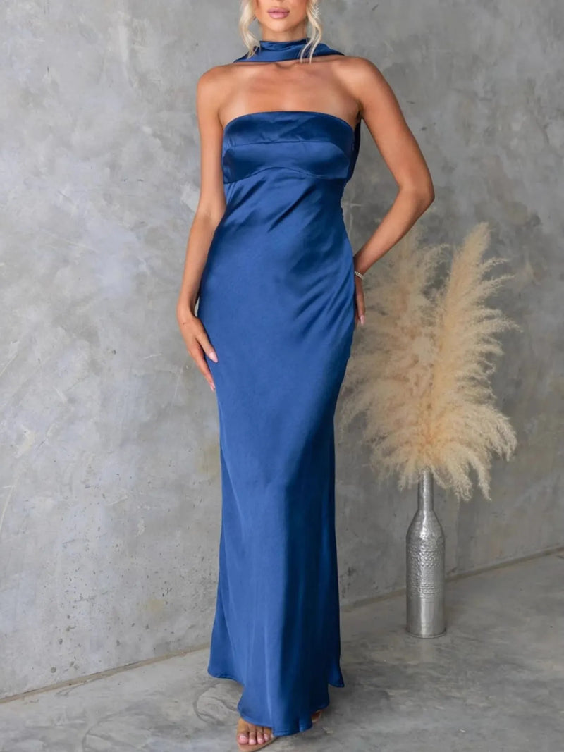 Woman wearing a blue halter neck gown against a gray concrete wall.