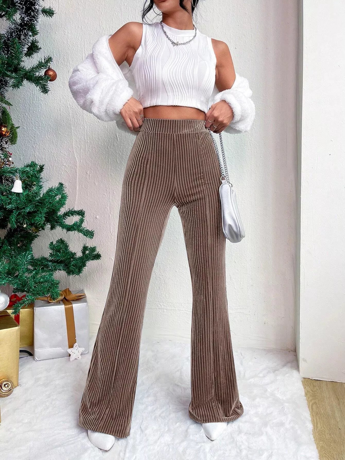 Woman wearing a white top and brown ribbed pants in a festive setting with a Christmas tree.