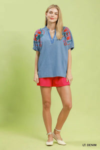 Woman wearing a light denim top with colorful embroidery and pink shorts on a green background