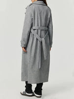 Person wearing a long gray coat with a belt on a white background