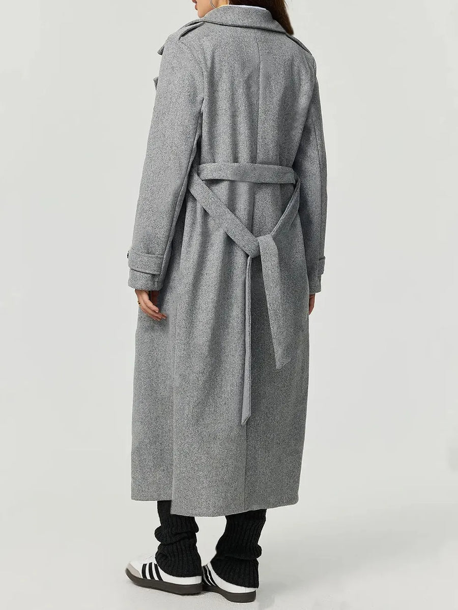 Person wearing a long gray coat with a belt on a white background