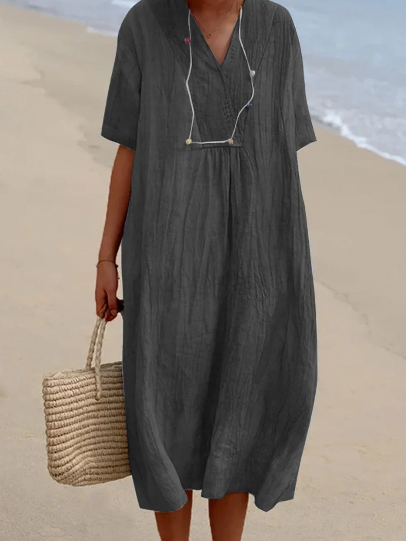 Person wearing a gray dress on a beach with a straw bag.