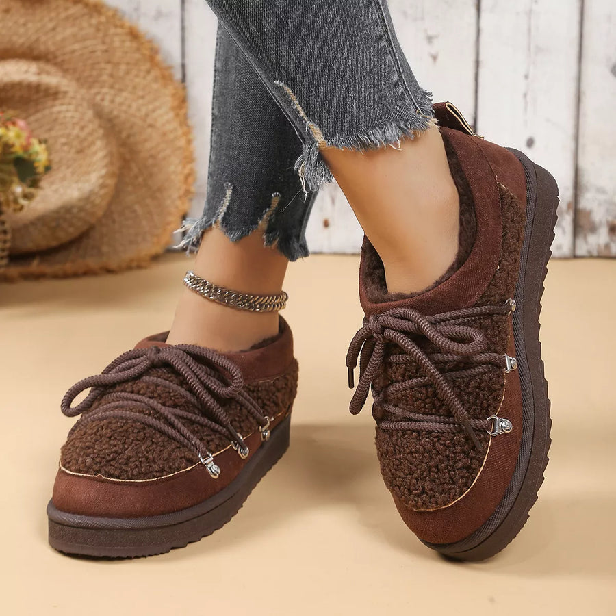Brown fuzzy shoes worn with ripped jeans on a wooden floor.