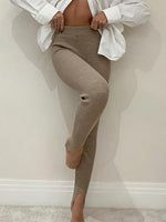Person wearing brown ribbed leggings and a white shirt against a plain wall.